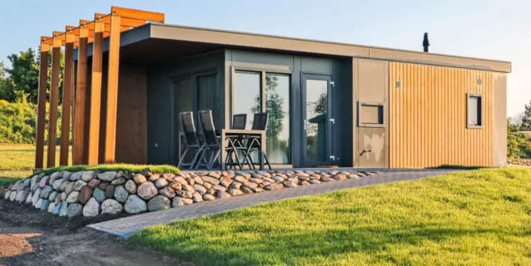 modernes Chalet in Süsel Seeparx aus hellem Holz kombiniert mit Grauen Wandelementen,bodentiefer Fensterfront sowie teilüberdachter Terrasse, Tisch und vier Stühlen