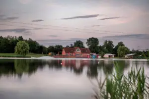 Blick über den See Süsel Seeparx im rosa Morgenlicht auf das Haus, die Seeterrasse und den Start einer Seilbahn sowie ein Feature